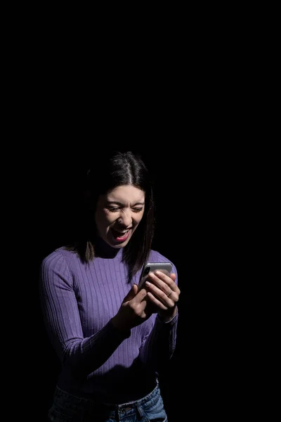 angry brunette woman looking at the mobile with a black background