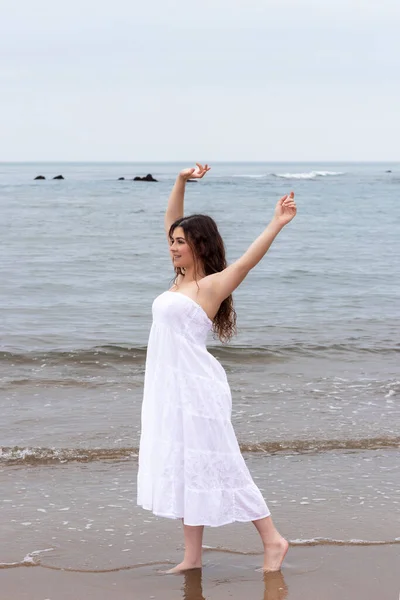 若いブルネットの女性が白いドレスでビーチで腕を上げて — ストック写真