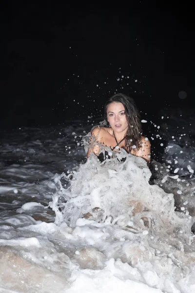 波が夜に飛び散っている間に海の中でひざまずいて楽しいフィット若い美しさの女性モデル — ストック写真