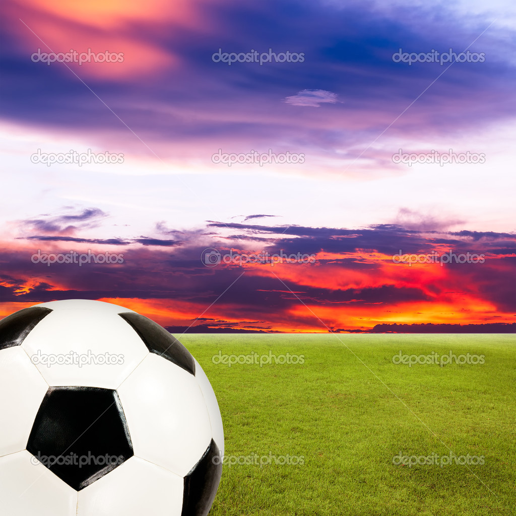 soccer ball with green grass field against sunset sky