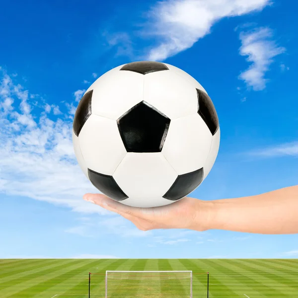 Pallone da calcio in mano con campo da calcio e cielo blu — Foto Stock