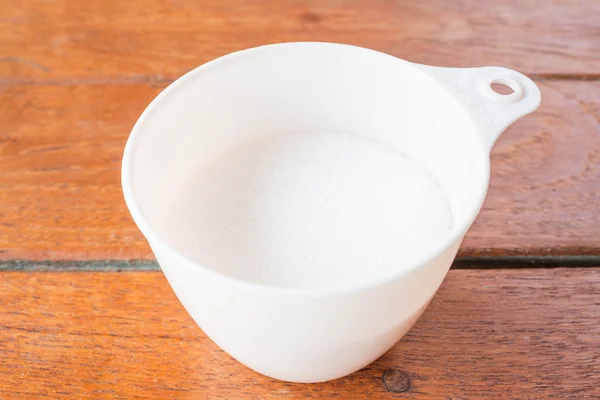 Bakery white sugar measured in plastic cup — Stock Photo, Image
