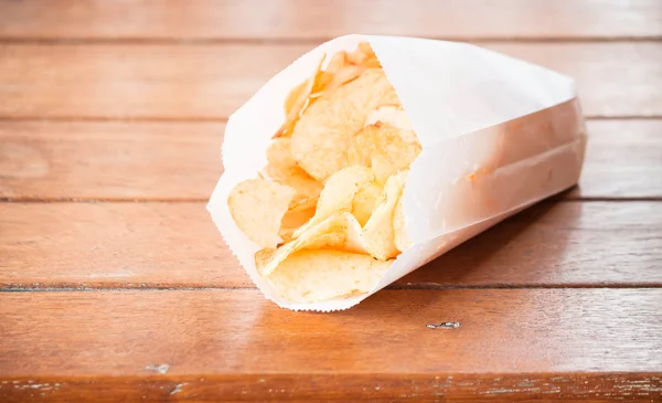 Kartoffelchips in Papiertüte auf Holztisch — Stockfoto