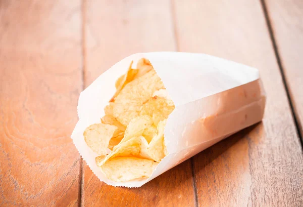 Kartoffelchips in Papierverpackung auf Holztisch — Stockfoto