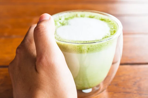 Hand on hot matcha green tea latte glass — Stock Photo, Image