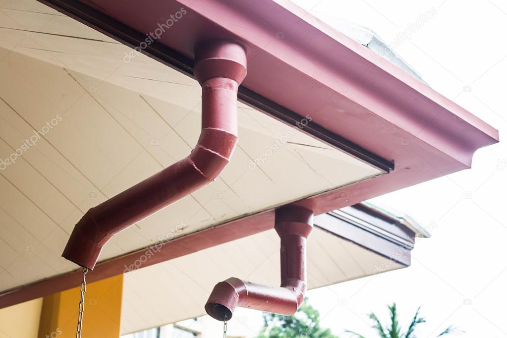 Corner of house with rain gutters on sky background
