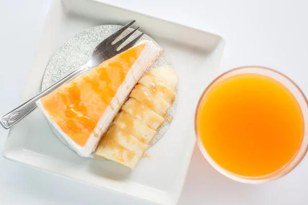 Top view of banana caramel crepe cake and orange juice on white — Stock Photo, Image