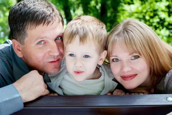 Famille souriante heureuse dans un parc, assise sur un banc — Photo