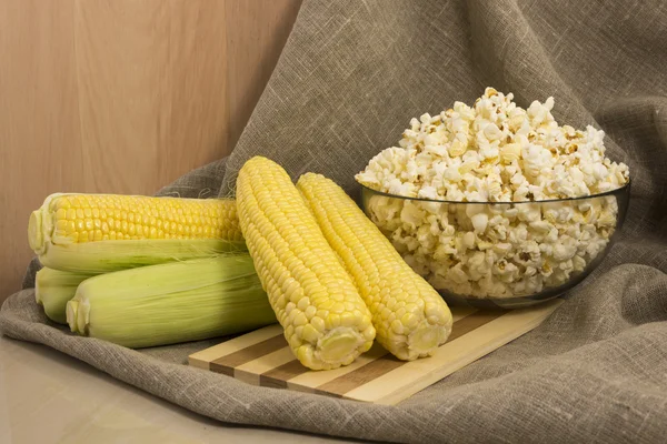 Corn on the cob and popcorn in a glass bowl — Stock Photo, Image