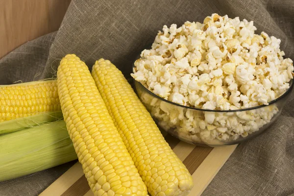 Corn on the cob and popcorn in a glass bowl — Stock Photo, Image