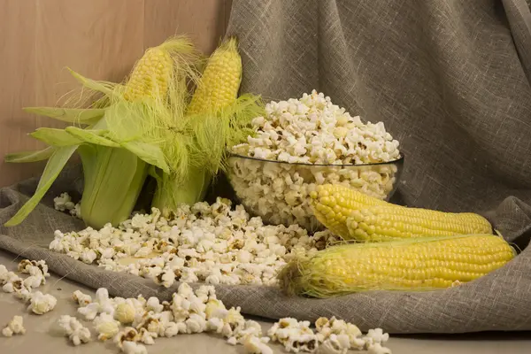 Corn on the cob and popcorn in a glass bowl on the table — Stock Photo, Image