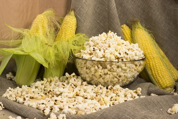 Corn on the cob and popcorn in a glass bowl on the table — Stock Photo, Image