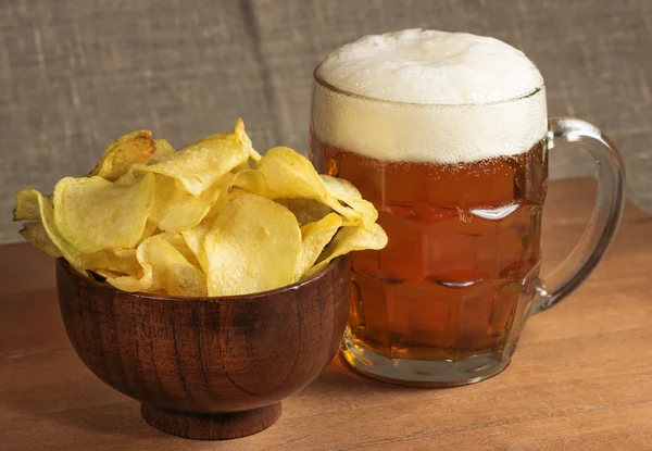 Potato chips in a wooden bowl and mug of beer on the table — Stock Photo, Image