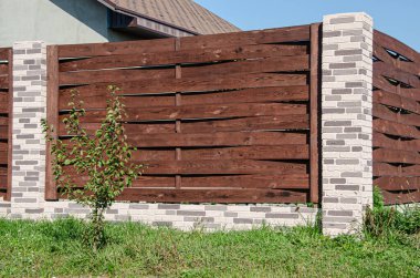 Bahçeli bir konut binasının yanında tuğla direkli dekoratif beton çitler..