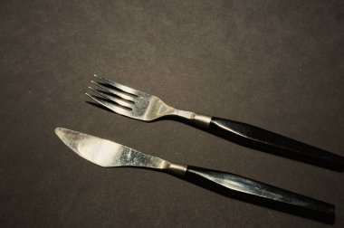 Çatal ve bıçak. Siyah mutfak gereçleri siyah bir masaya yerleştirilmiş. Üst görünüm düz yüzey ve kopyalamak için boşluk