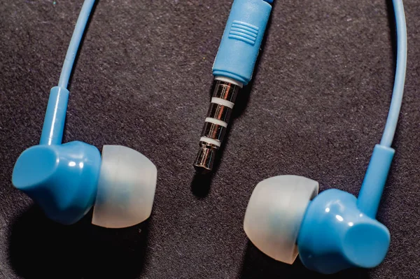 Tek renkli siyah bir yüzeye yakın plan mavi kablo kulaklıklar. Bir cep telefonu için kulaklık.