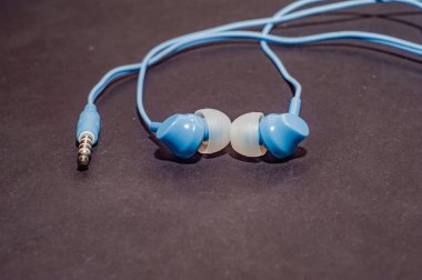 Tek renkli siyah bir yüzeye yakın plan mavi kablo kulaklıklar. Bir cep telefonu için kulaklık.