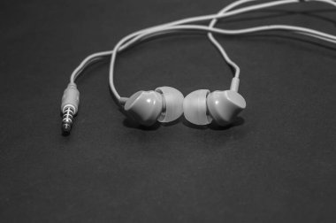 Tek renkli siyah bir yüzeye yakın plan beyaz kablo kulaklıklar. Bir cep telefonu için kulaklık. Müzik