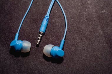 Tek renkli siyah bir yüzeye yakın plan mavi kablo kulaklıklar. Bir cep telefonu için kulaklık.