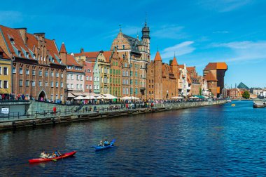 Gdansk 'taki Motlawa Nehri' nin seti. Eski tuğla evler ve vinç. Motlawa Nehri boyunca kano üzerinde yüzen turistler