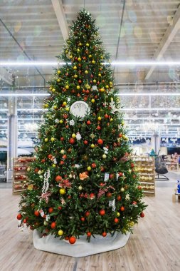 Noel ağacı pelerinlerle süslenmiş, renkli oyuncaklar, çelenkler ve kış tatili için mağazada ışıklar. Pullu çelenklerle bulanık bir arkaplan. yumuşak odak.                               