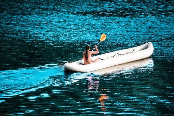 A sports girl in a swimsuit is riding an inflatable boat on the lake. A girl in an inflatable kayak rowing quickly with an oar. Sports water activities and water sports
