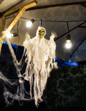 Cadılar Bayramı 'nda bir ışık çelenginin yanında örülmüş bir iskelet ve örümcek ağları asılı duruyor. Azizlerin, cadılar bayramının ve ölmüş ruhların günü için ev dekorasyonu. Ölüler Günü için dekoratif alan                               