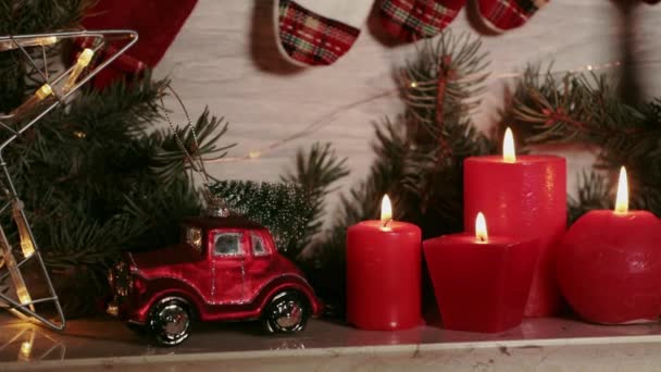 赤いキャンドルクリスマスのおもちゃは マントルピースクリスマスイブ 屋根にクリスマスツリーがある赤い車 緑のトウヒの枝 燃えるろうそく アドベントカレンダー ガーランドライト — ストック動画