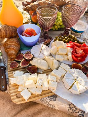 Çeşitli peynirler, zeytinler, poidolar, üzümler, kruvasanlar, incirler ve kumsalda bir bardak şarapla şenlik partisi. Kumsalda peynirler ve meyvelerle Sevgililer Günü pikniği