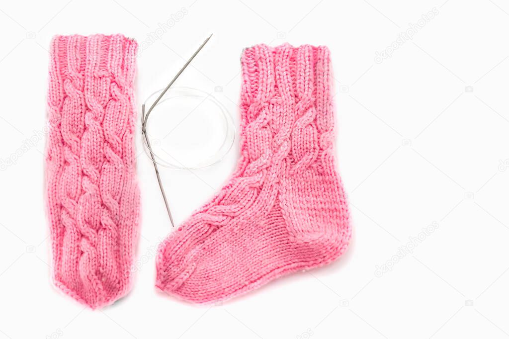 Pink knitted socks with Aran pattern and knitting needles on a white background. Place for text. Warm handmade knitted socks with beautiful patterns. Traditional crafts for psychological rehabilitation