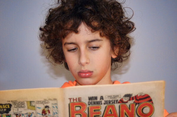 Young boy is reading a British comic magazine called Beano