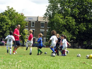 Çocuklar parkta futbol oynuyor.