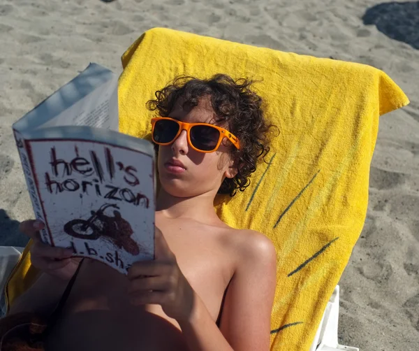 Jonge jongen leest boek op het strand — Stockfoto