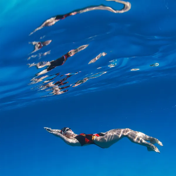 Professional female swimming on back underwater in blue water — Stock Photo, Image