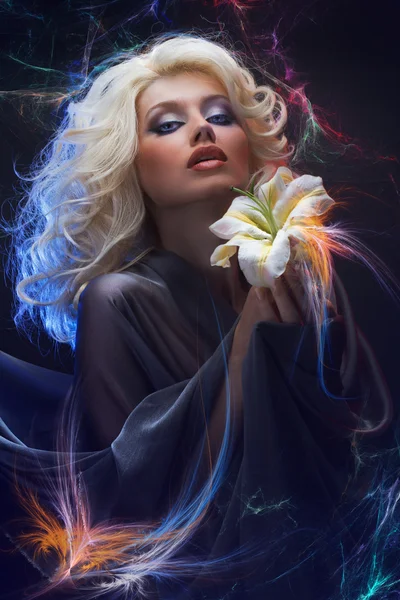 Attraktive Blondine mit blauen Augen trägt graues Seidenkleid und hält weiße Lilie an beiden Händen auf schwarzem Hintergrund — Stockfoto