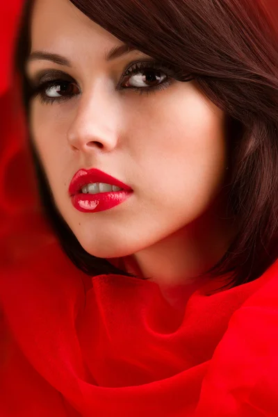 Beautiful face with red sweet lips in the folds of red cloth — Stock Photo, Image