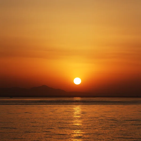 Naranja puesta de sol en el mar con siluetas de montañas en horizontal — Foto de Stock