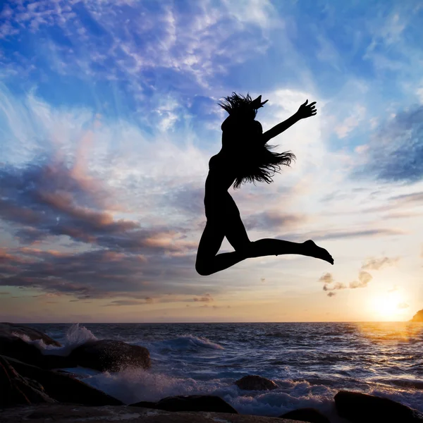 Solnedgång på bakgrunden stranden med havet vågor och långhåriga flicka hoppande — Stockfoto