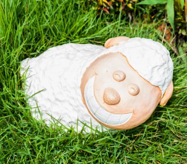 Yeşil çimenlerin üzerinde gündüz beyaz bir gülümseme koyun heykeli