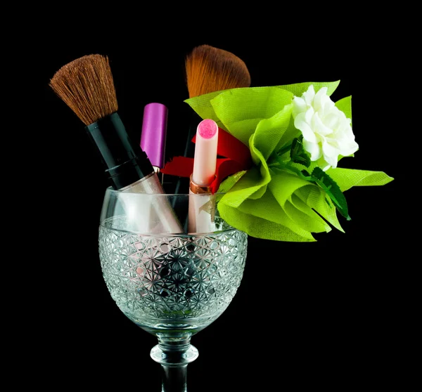 Bicchiere di cristallo di vino con pennelli e cosmetici di trucco isolati su nero - set di cosmetici in vetro di cristallo — Foto Stock