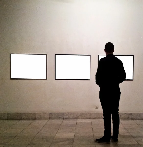 Человек в галерее смотрит на пустые рамы — стоковое фото