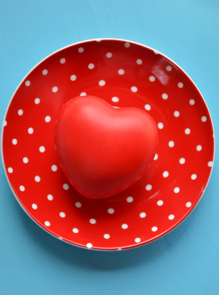 Corazón sobre plato rojo de lunares sobre fondo azul — Foto de Stock