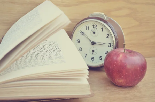 Открытая книга и красное яблоко на деревянном столе — стоковое фото