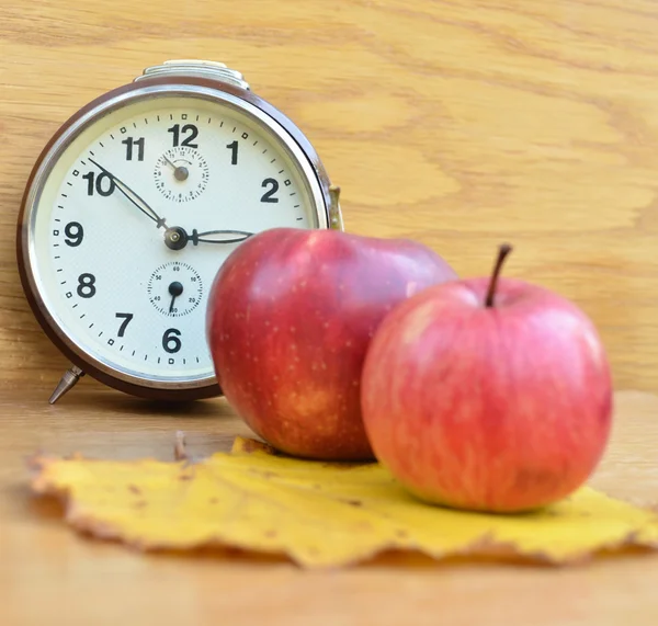 Czerwone jabłka i zegar na drewnianym stole — Zdjęcie stockowe