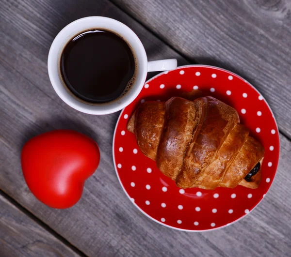 Red cup of coffee and croissant with heart — Stock Photo, Image