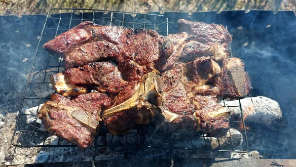 Kömürde pişirilmiş iki parça biftek. Biftek ızgaranın ızgarasında pişiyor.