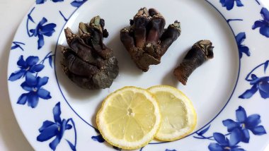 Bir grup Percebe ya da kaz boyunlu, beyaz tabakta limonlu deniz ürünleri.