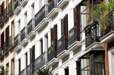   The facade of typical Spanish old house with beautiful balcony with various green plants in summer. Balcony with metal railings.                            