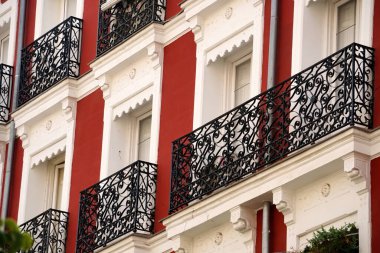  The facade of typical Spanish old house with beautiful balcony with various green plants in summer. Balcony with metal railings.                            