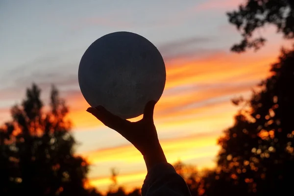 Moon in the hand on red sunrise background. Moon bedside lamp on the sky